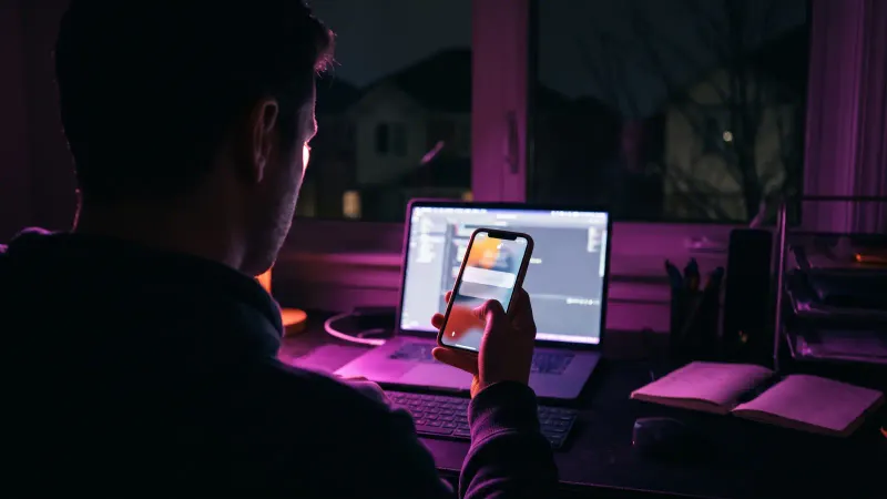 Silhouette at a home desk late at night holding a lit phone, the after hours response an MDR agreement should define