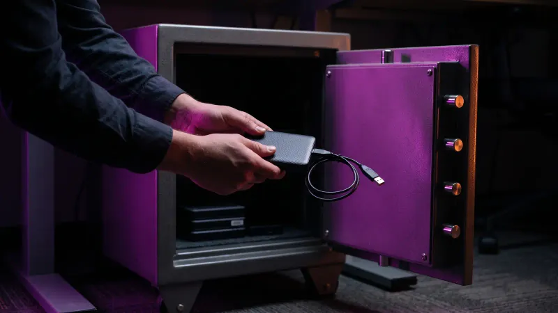 Hands placing an unplugged backup drive into a fireproof safe, keeping a small business backup away from ransomware